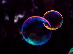 Two luminescent bubbles in blue, pink, and gold are floating. A larger one on the left and a smaller bubble disconnecting on the right.
