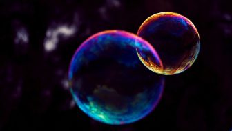 Two luminescent bubbles in blue, pink, and gold are floating. A larger one on the left and a smaller bubble disconnecting on the right.