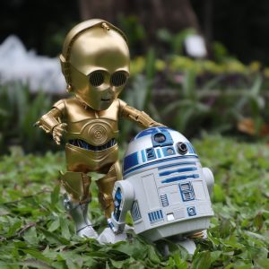 Cute small baby versions of R2D2 in silver metal and C-3PO in fold metal from Star wars standing on green leaves