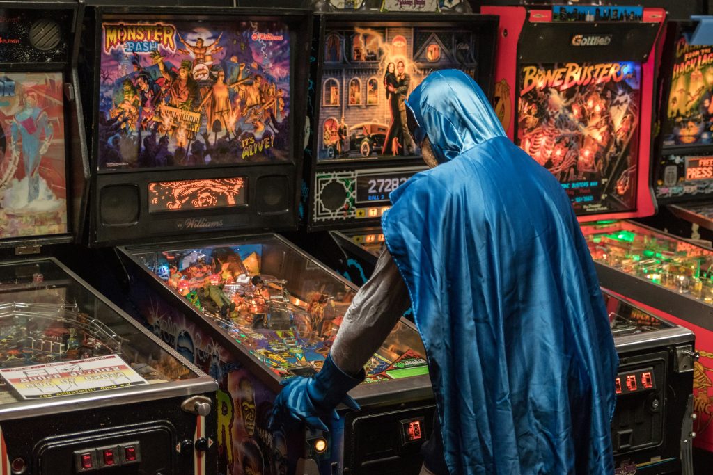 Batman wearing a blue cape playing Monster Bash Pinball machine