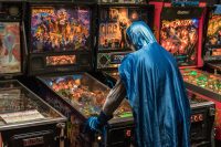 Batman in a blue cape playing pinball on a monster bash pinball machine